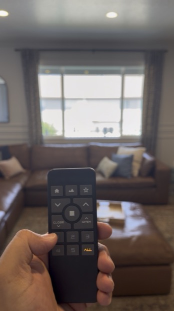 Hand holding a remote that operates motorized shades in a living room